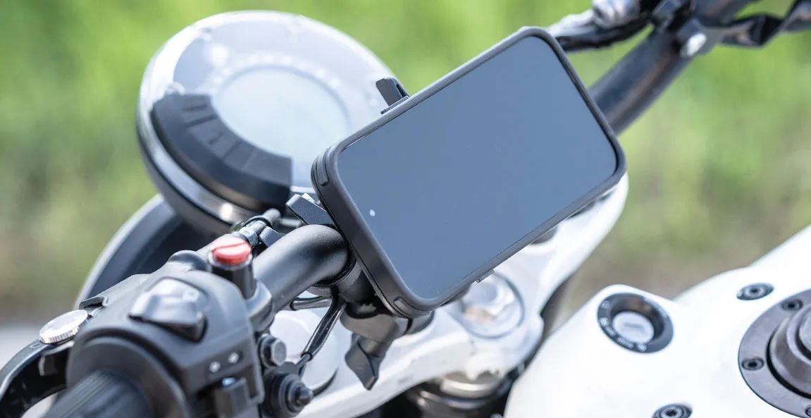 Un motociclista utilizza un smartphone come navigatore, con un supporto posizionato sul manubrio, mentre attende il verde al semaforo